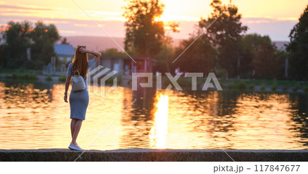 Young woman in casual outfit relaxing on lake side on warm evening. Summer vacations and travelling concept. Young woman in casual outfit relaxing on lake side on warm evening. Summer vacations and travelling concept. 117847677