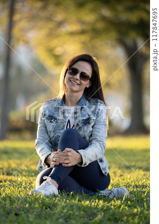 Woman sitting on grass in city park on summer day Woman sitting on grass in city park on summer day 117847695