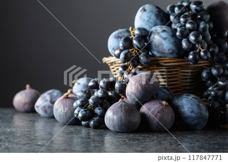 Blue grapes, blue plums, and figs on a black stone table. 117847771