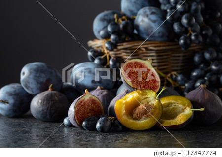 Blue grapes, blue plums, and figs on a black stone table. 117847774