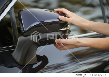 Driver hands adjusting side view mirror of a car 117847783