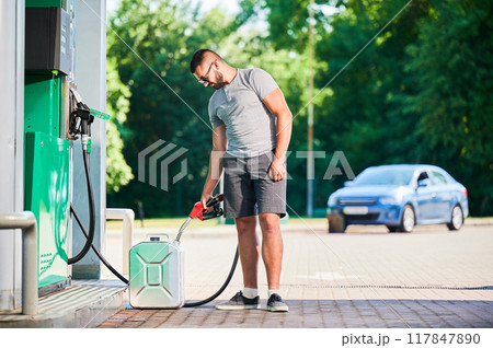 Driver refueling canister with gasoline at modern gas station. Man filling cistern with fuel in case of unforeseen circumstances. Man in casual clothes with pump nozzle on background of his car. 117847890