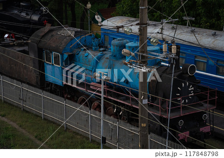 An old, blue, abandoned steam locomotive stands in a depot in the city An old, blue, abandoned steam locomotive stands in a depot in the city 117848798