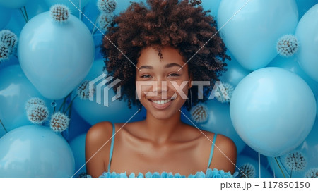 Happy birthday. A woman in her thirties with an Afro wearing light blue dress, celebrating birthday party surrounded by pastel blue balloons. The background is a solid vibrant sky-blue color. 117850150