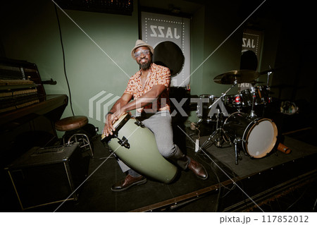 Flash photo of African American musician posing for camera with conga on stage in local bar Flash photo of African American musician posing for camera with conga on stage in local bar 117852012