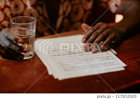 Closeup of unrecognizable African American musician sitting in bar with sheet music on wooden table 117852020