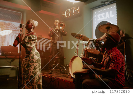 Group of four young professional musicians playing instruments and singing in Afro-Cuban jazz band on stage in local bar 117852050
