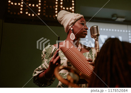 Medium low angle view shot of young African American woman singing jazz song and playing guiro 117852084