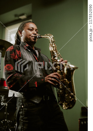 Vertical medium long low angle view of young Black jazz musician playing saxophone on stage 117852090