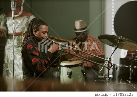 Young African American man with long dreadlocks playing trombone in jazz band on stage in bar Young African American man with long dreadlocks playing trombone in jazz band on stage in bar 117852123
