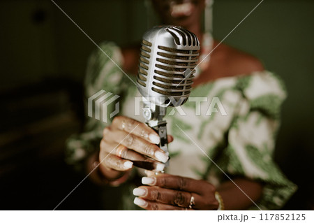 Unrecognizable Black female singers hands adjusting microphone for performance, closeup shot 117852125