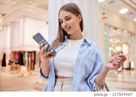 Young beautiful lady checking her phone during doing shopping in mall Young beautiful lady checking her phone during doing shopping in mall 117854507