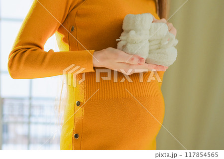 Pregnancy motherhood people expectation future. Big belly of pregnant woman, newborn baby booties in hands close up. Mom enjoying pregnancy relaxing at home. Maternity tenderness parenthood new life Pregnancy motherhood people expectation future. Big belly of pregnant woman, newborn baby booties in hands close up. Mom enjoying pregnancy relaxing at home. Maternity tenderness parenthood new life 117854565