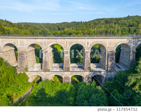The Sychrov Railway Bridge rises gracefully above lush greenery, showcasing its impressive arches against a backdrop of vibrant trees. 117854732
