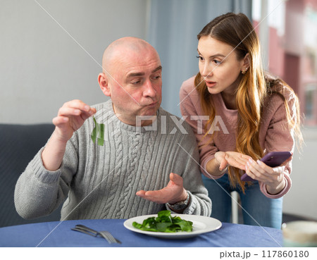 Wife with smartphone explaining health benefits of salad to her husband 117860180
