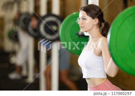 Young woman lifting barbell in gym Young woman lifting barbell in gym 117860297