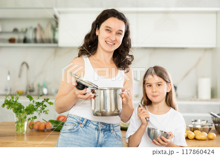 Mom and little daughter are standing at kitchen table with dishes in their hands. Mom and little daughter are standing at kitchen table with dishes in their hands. 117860424