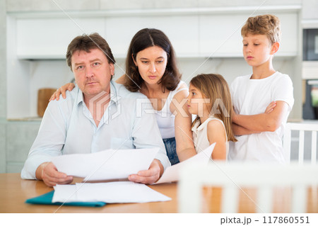 Wistful father looking through papers with family 117860551