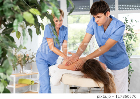 Young masseur in tandem with female colleague performing back massage to woman 117860570