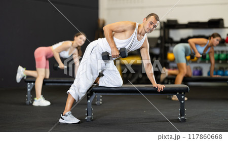 Young man training with dumbbells on bench 117860668