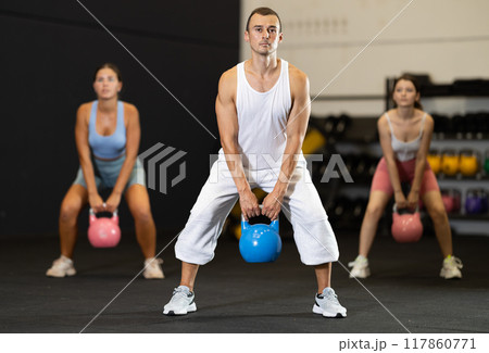 Sportive male in activewear swinging kettlebell during group exercise class in crossfit gym indoors 117860771
