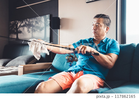 休日に自宅で釣り竿のメンテナンスをする男性 117862165