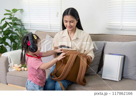 Asian girl wearing headphones while mother organizes school items Asian girl wearing headphones while mother organizes school items 117862166