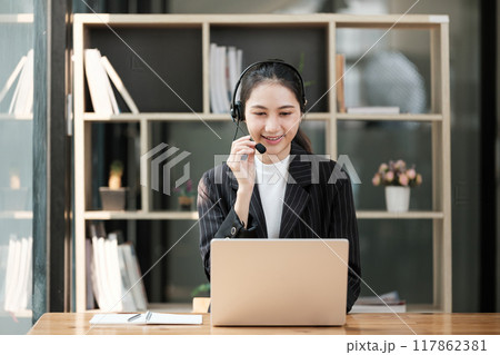 A woman is sitting at a desk with a laptop and headset on A woman is sitting at a desk with a laptop and headset on 117862381