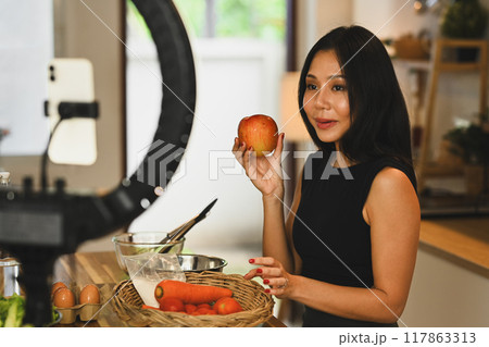 Young female influencer vlogging about healthy eating from her kitchen. Healthy lifestyle vlogs concept Young female influencer vlogging about healthy eating from her kitchen. Healthy lifestyle vlogs concept 117863313