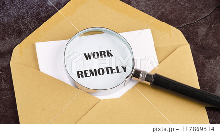 Networking, communication and person on computer for planning, online discussion. WORK REMOTELY written through a magnifying glass in a letter on white paper sticking out of an envelope 117869314