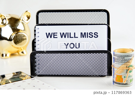 WE WILL MISS YOU written in a notebook in a stand on a white background 117869363
