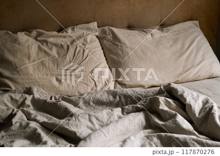 Empty bed covered wrinkled bedding and pillows in cozy bedroom at nighttime. 117870276