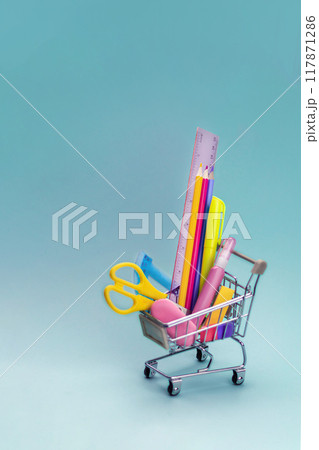 Supermarket trolley with school or office stationary isolated on an blue background. Free space for your text, copy space vertical Supermarket trolley with school or office stationary isolated on an blue background. Free space for your text, copy space vertical 117871286