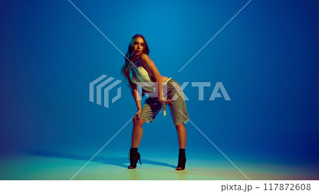 Sensual young beautiful woman dancing high heel dance, performing against blue studio background in neon light Sensual young beautiful woman dancing high heel dance, performing against blue studio background in neon light 117872608