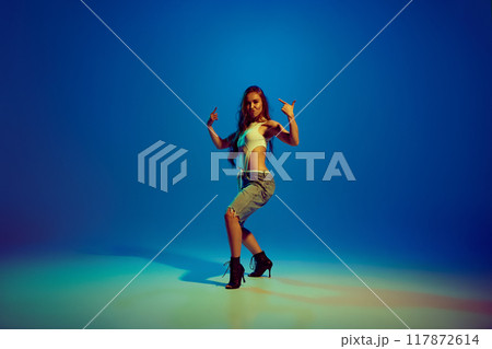 Passionate woman, elegant dancer in mix of sport and romantic clothes dancing on heels against blue studio background in neon light Passionate woman, elegant dancer in mix of sport and romantic clothes dancing on heels against blue studio background in neon light 117872614