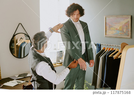 Unrecognizable tailor touching suits sleeve while model standing still 117875168