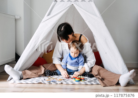 Mother playing with toddler in makeshift indoor tent. Early childhood development, role of play, motor skills, cognitive growth, parent-child interaction Mother playing with toddler in makeshift indoor tent. Early childhood development, role of play, motor skills, cognitive growth, parent-child interaction 117875876