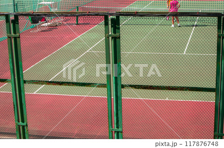 A tennis court behind a metal fence made of armored mesh in the open. The concept of a sports activity in summer 117876748
