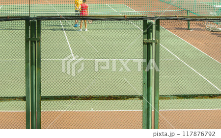 A tennis court behind a metal fence made of armored mesh in the open. The concept of a sports activity in summer A tennis court behind a metal fence made of armored mesh in the open. The concept of a sports activity in summer 117876792