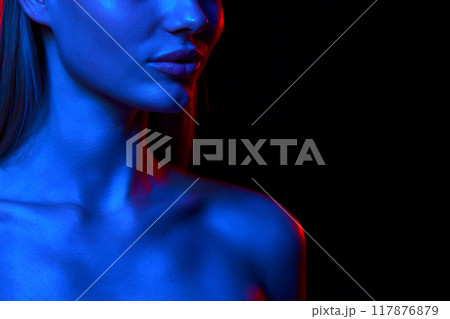 Cropped image of beautiful young woman, shoulders, demonstrating perfect facial lines against black studio background in neon light Cropped image of beautiful young woman, shoulders, demonstrating perfect facial lines against black studio background in neon light 117876879