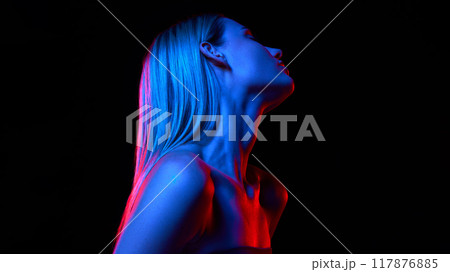 Woman with perfect long hair and bare shoulders against black studio background in neon light. Dedicated care and cosmetics 117876885