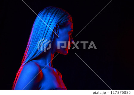 Woman with perfect long hair and bare shoulders against black studio background in neon light. Dedicated care and cosmetics 117876886
