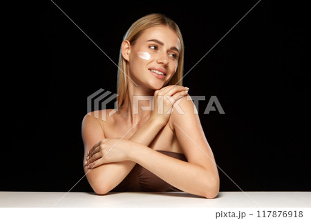Radiant young woman with clear skin applying face cream, demonstrating role of effective skincare products in achieving smooth, glowing complexion. 117876918