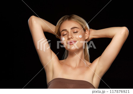 Beautiful woman with perfect complexion gently applying face cream isolate don black background. Effectiveness of quality cosmetics 117876921