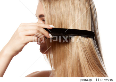 Stunning young woman with flawless blonde hair, brushing straight hair isolated on white studio background. Effective hair care and cosmetics. 117876940