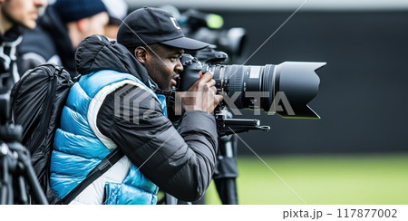Focused and engaged sports photographer in action, capturing moments with large telephoto lens camera. 117877002