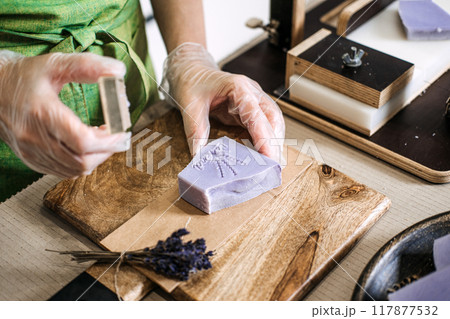 Close-up of hands pressing handmade lavender soap with floral stamp. Natural skincare, artisan soap making, organic beauty, sustainable living, eco-friendly concept 117877532