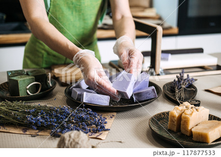 Hand arranging lavender handmade soap bars with dried lavender. Soap making, organic skincare, small business, natural cosmetics, DIY beauty, sustainable living concept 117877533