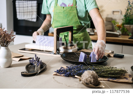 Artisan hands cutting handmade lavender soap block with wire slicer. Soap making, craftsmanship, organic skincare, natural cosmetics, DIY beauty, sustainable living concept Artisan hands cutting handmade lavender soap block with wire slicer. Soap making, craftsmanship, organic skincare, natural cosmetics, DIY beauty, sustainable living concept 117877536