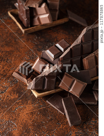 Broken bitter and milk chocolate bars on a brown background. 117878865